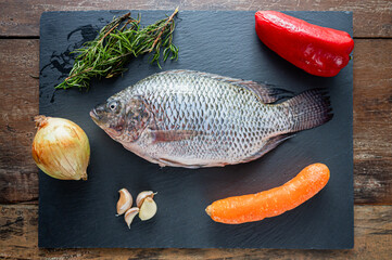Fresh mojarra fish ready for cooking with vegetables and herbs on slate