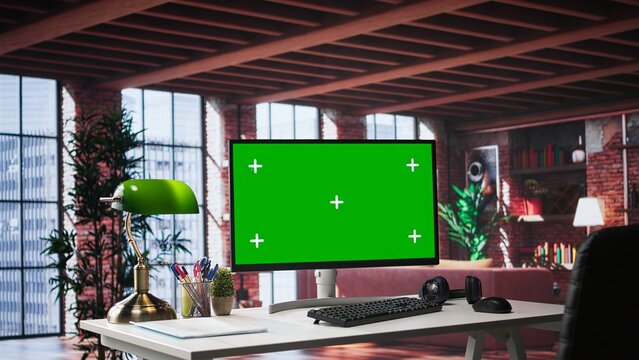 Refined office setup in classy loft with green screen monitor for mockups use. Chic interior design and upscale furniture reflect a serene, creative and exclusive environment. Spacious home.