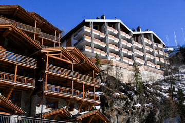 Obraz premium Traditional wooden alpine chalets and a modern mountain lodge located on a steep slope in Zermatt, Switzerland. Clear blue sky and winter daylight atmosphere.