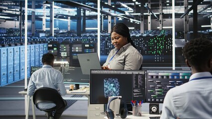 Data center admin using laptop to do node tree programming, optimizing resource allocation. Woman in server room uses predictive AI visualization systems on notebook for maintenance planning, camera A