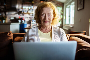 Senior woman smiling while using laptop at home