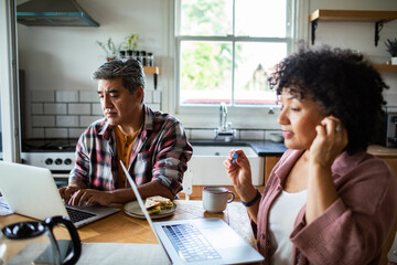 Adult couple focused on laptops at home kitchen