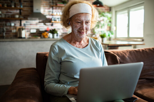 Senior woman smiling with facial mask using laptop at home