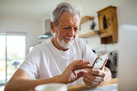 Senior man smiling while using smartphone at home kitchen