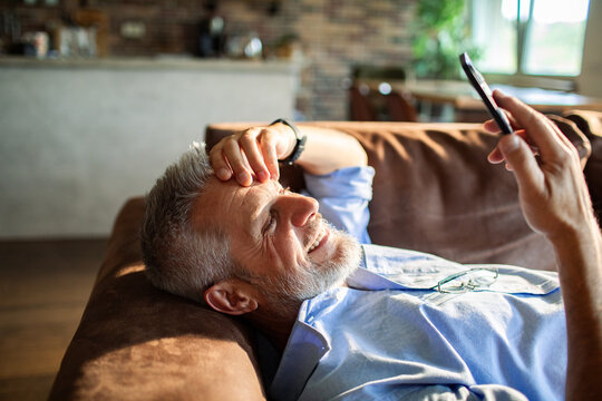 Mature man smiling at smartphone on sofa at home