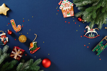 Christmas flat lay frame with gingerbread cookies and ornaments on dark blue background.