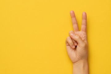 Naklejka premium Hand is holding up two fingers in a peace sign. The yellow background adds a warm and inviting atmosphere to the image