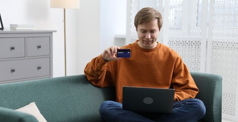 Young man making online payment with laptop and credit card indoors, space for text