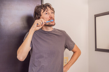 Man brushing his teeth in a modern bathroom, practicing daily hygiene and morning self-care routine. Healthy lifestyle, grooming, cleanliness and dental care concept