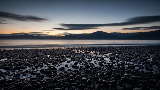 Dark, moody seascape at twilight showing a rocky beach foreground and distant mountain silhouette - Powered by Adobe