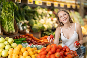 Young woman buyer choosing fresh tomatoes in vegetable shop