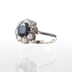 18kt white gold ring with central sapphire and brilliant-cut diamonds, photographed on a white background with reflection