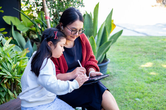 Mother and daughter using digital tablet together outdoors, focusing on learning and creativity in a natural garden setting, showing modern education, bonding and family lifestyle and connection. - Powered by Adobe