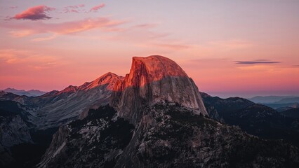 Naklejka premium Landscape of a mountain at sunset with a pink-orange sky and rugged terrain.