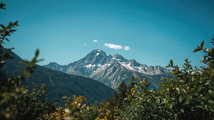 Obraz premium A mountain landscape with snow-capped peaks and green forests, under a blue sky with clouds.