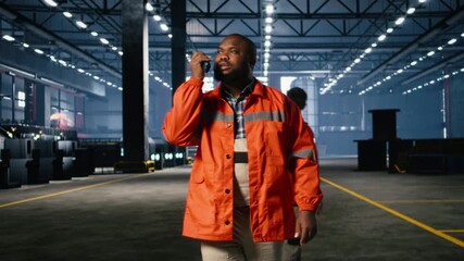 Black worker uses walkie talkie radio to guide colleague personnel on the factory floor, highlighting communication, manpower and operation structure in busy industrial plant. Camera A.