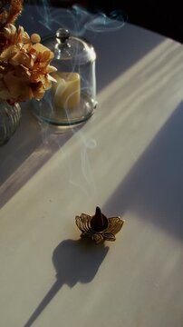 9x16 vertical close-up of smoke rising from a burning incense cone by a sunlit window on an autumn morning, with flowers on the table creating a serene, meditative, calming mood.