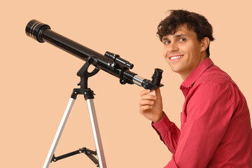 Young man with telescope on beige background