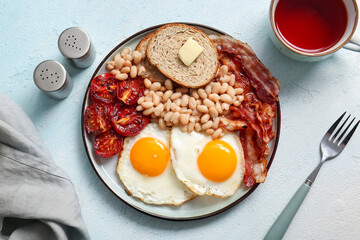 Plate with tasty English breakfast and cup of tea on blue background