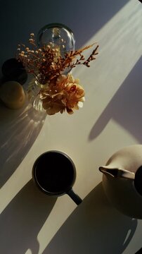 Top-down vertical shot of a relaxing morning tea ceremony as a woman&rsquo;s hands pour tea from a ceramic pot, softly lit by the sun, with steam rising and glowing in the backlight.