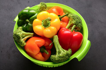 Colander with different fresh vegetables on black background