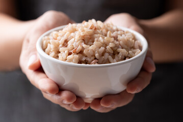 Cooked Thai brown rice in a bowl holding by hand, Healthy eating