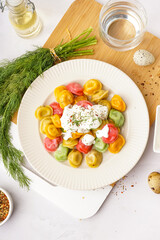 Plate of boiled colorful dumplings with sour cream and dill on white background