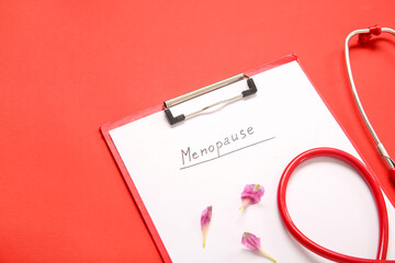 Clipboard with word MENOPAUSE, floral petals and stethoscope on red background, closeup