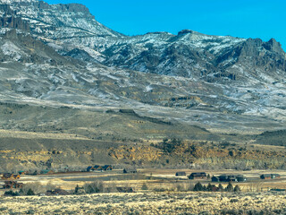 Mountain scenery near Cody, Wyoming, in Wapiti Valley, shows homes below snowy mountains. Size comparison is amazing & emphasizes vast  outdoor beauty. large home was removed with AI