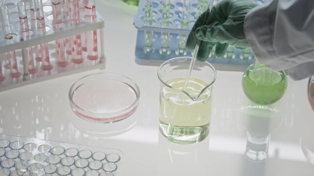 High angle close-up shot of unrecognizable scientist in gloves stirring chemical liquid in sterile laboratory