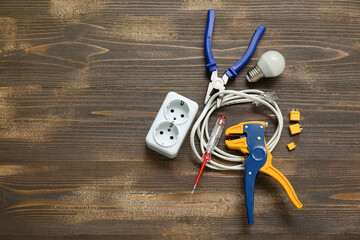 Electrician's tools, cable, socket and light bulb on wooden background