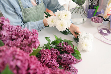 Female florist with lilacs and chrysanthemum for bouquet in flower shop