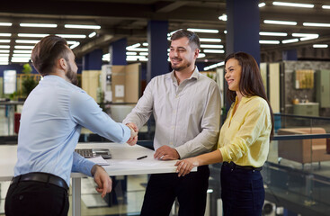 Friendly furniture shop consultant exchanges handshakes with customers. Happy couple shake hands...
