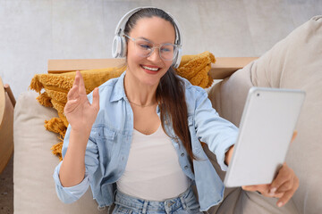 Young woman in headphones with tablet computer video chatting on sofa at home