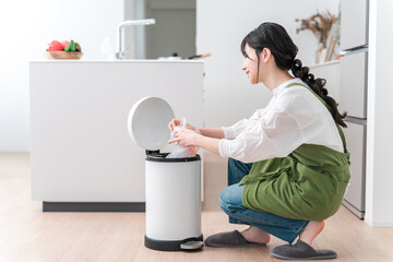 A woman in an apron collecting trash in the trash can in the kitchen, a housewife
