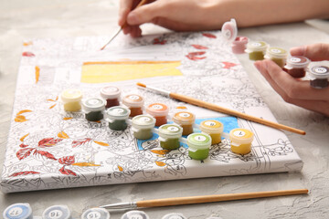 Woman paints on canvas for painting by numbers on grey grunge table