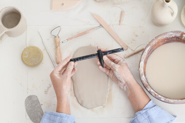Young female potter with pottery compass and clay slab in home studio, top view