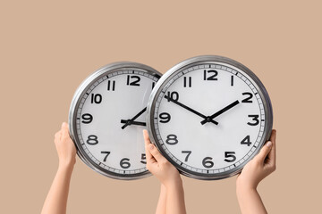 Female hands holding wall clocks on beige background