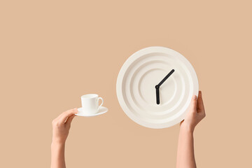 Female hands holding wall clock and cup of coffee on beige background