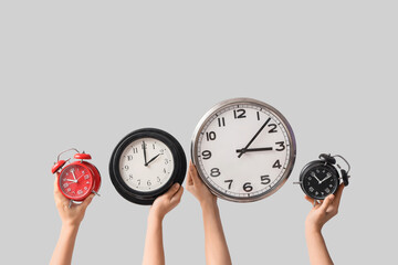 Female hands holding different wall and alarm clocks on grey background