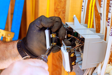 Skilled worker is installing circuit breakers in home, wearing gloves using drill tools