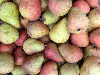 Close-up of a pile of fresh pears with green and reddish hues, creating a natural fruit background ideal for food, health, and organic produce concepts.