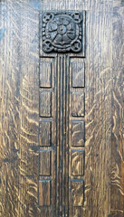 Close-up of an ornate carved wooden detail featuring a decorative floral motif and vertical rectangular patterns, showcasing rich texture and craftsmanship.