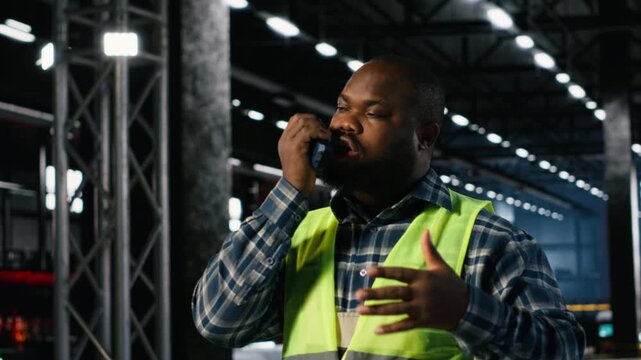 Black engineer talks into walkie talkie and supervising fabrication tools in a workshop, demonstrating strong labor involvement and development for activity within industry plant. Camera B.