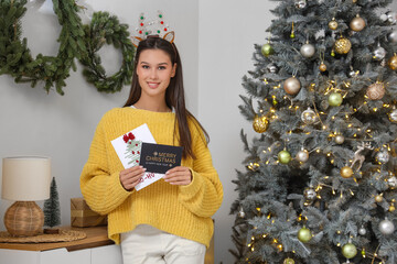 Beautiful young woman with Christmas greeting cards in festive room