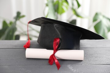 Diploma and graduation hat on grey wooden table indoors, closeup