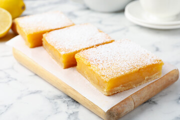 Tasty lemon bars with powdered sugar on white marble table, closeup