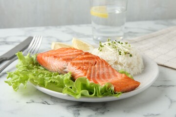 Piece of tasty grilled salmon, lemon, lettuce, rice and microgreens on light marble table against grey background, closeup