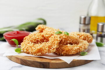 Deep fried squid rings, basil and ketchup on light marble table, closeup