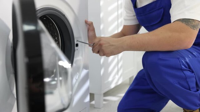 Repairman fixing broken washing machine with screwdriver at home, closeup. Camera moving forward